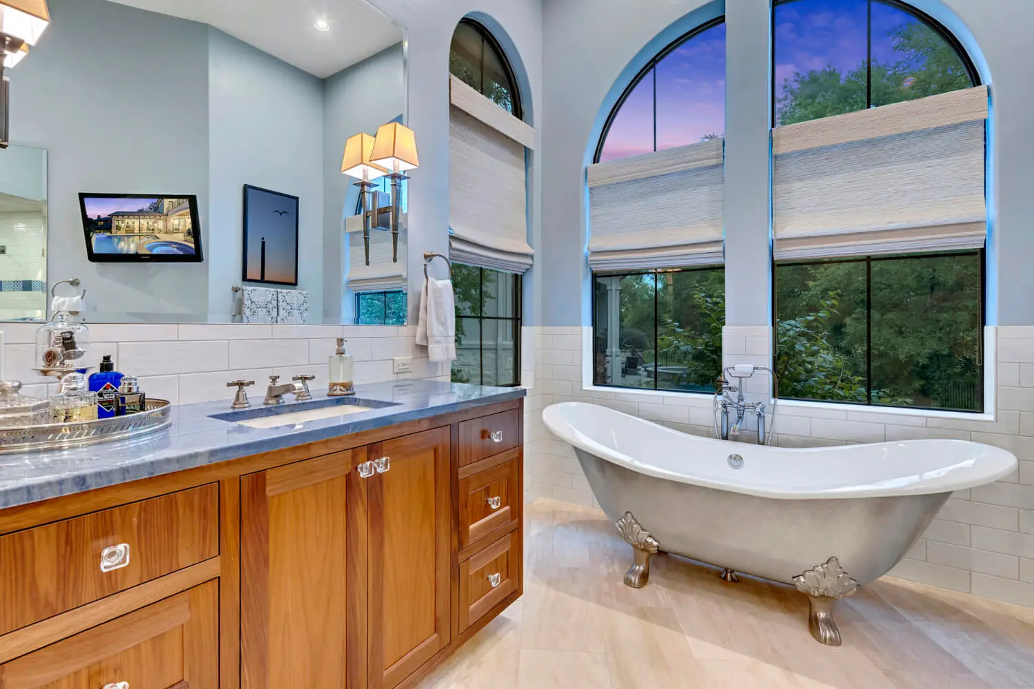 Aerial view at dusk of a tile-roofed home wrapped around a lit pool and spa, surrounded by oaks.