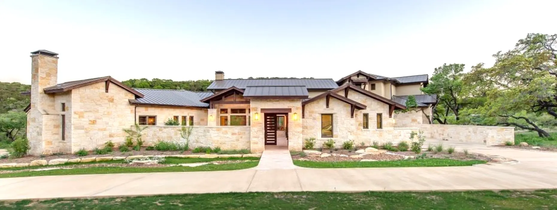 Front elevation of a single-storey limestone house with deep eaves, a metal roof and a straight walk to the entry.