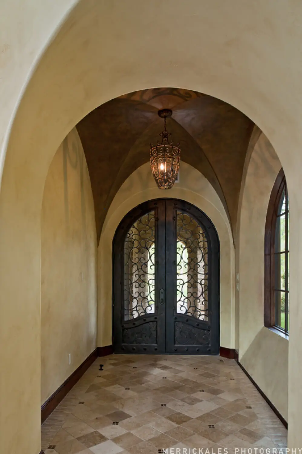 Front elevation at dusk of a stone and stucco home with a tile roof, lit entry arch and a flagstone walk across the lawn.