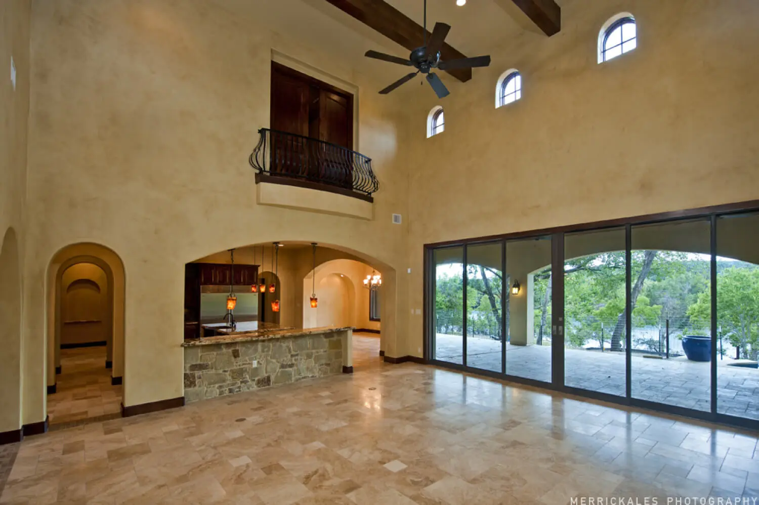 Front elevation at dusk of a stone and stucco home with a tile roof, lit entry arch and a flagstone walk across the lawn.