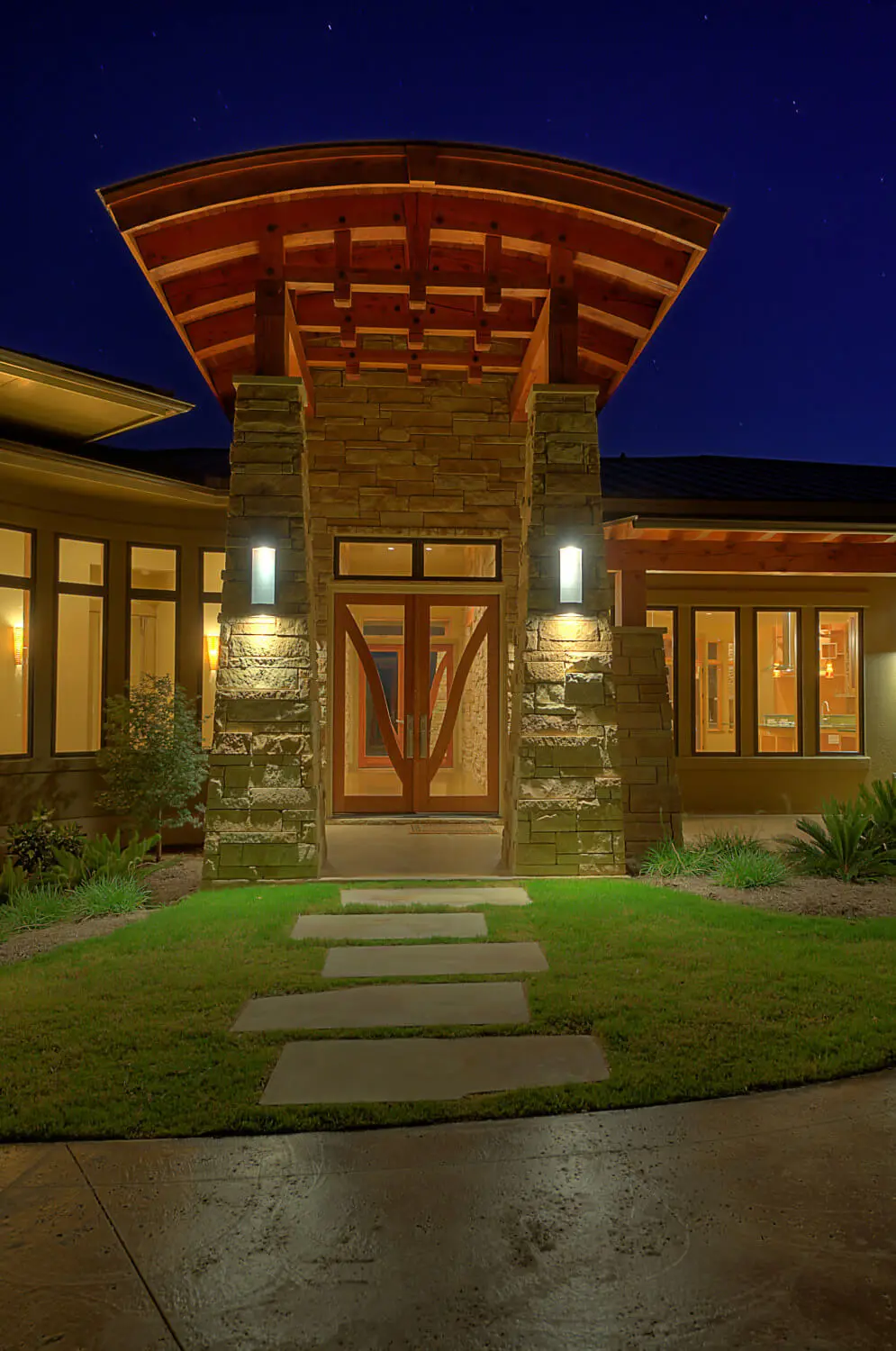 Long low home with a hipped metal roof and stone piers, seen across a lawn under a large live oak.