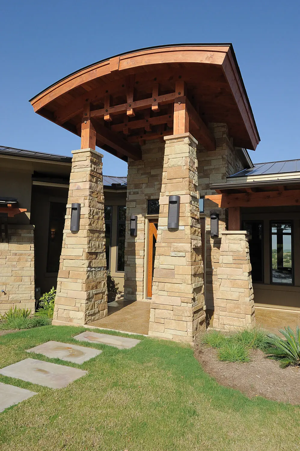 Long low home with a hipped metal roof and stone piers, seen across a lawn under a large live oak.