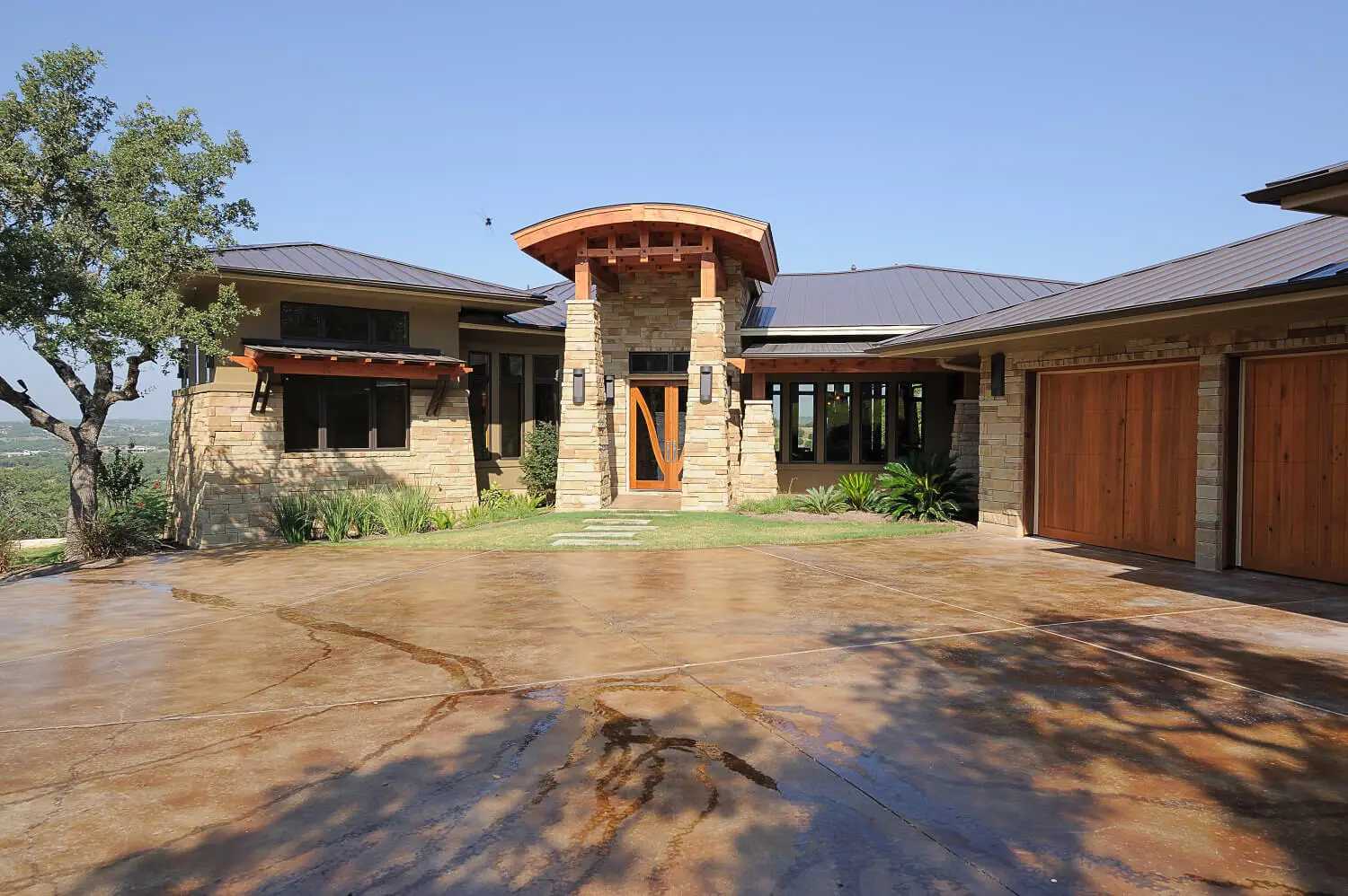 Long low home with a hipped metal roof and stone piers, seen across a lawn under a large live oak.