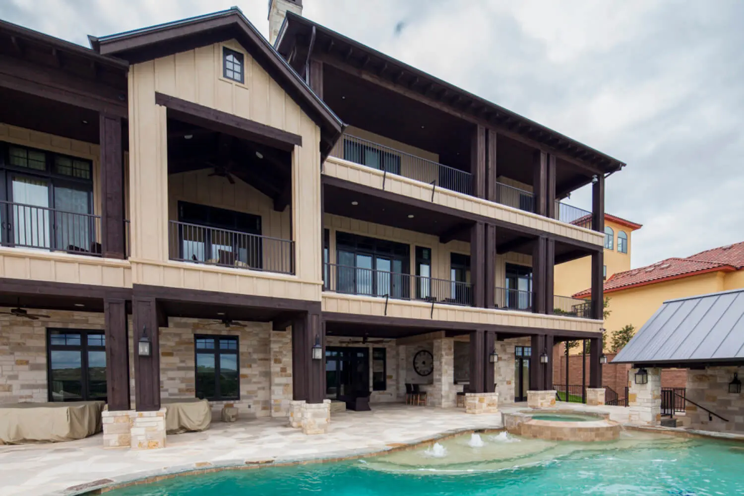 Rear elevation of a three-storey house with stacked timber balconies, above a pool and stone deck.